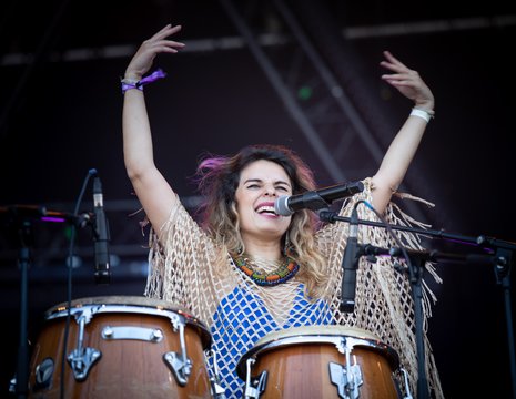 Une femme devant des percussions lève les bras en chantant